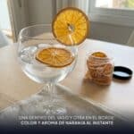 Copa de gin tonic con una rodaja de naranja deshidratada dentro y otra en el borde, junto al tarro abierto