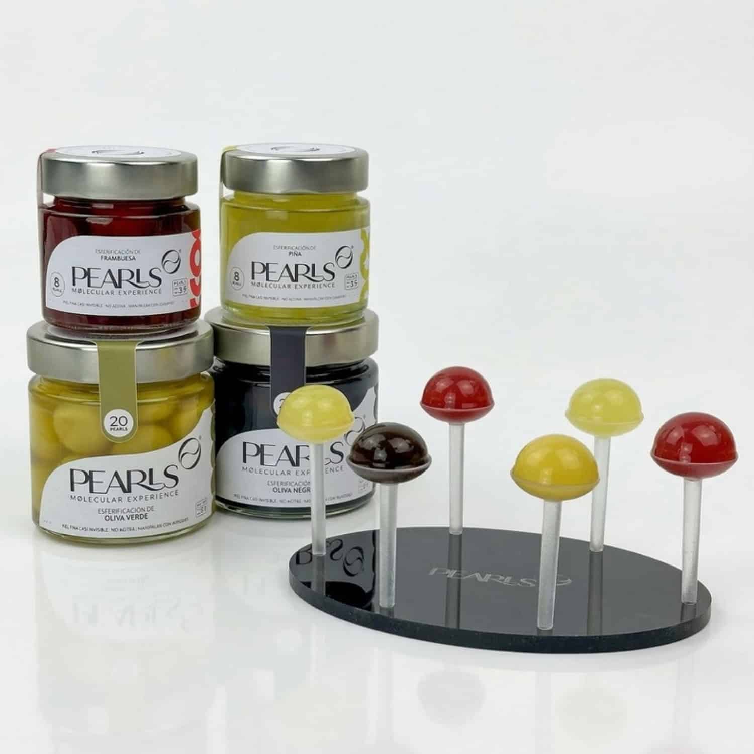 Tasting Pack Gourmet de Pearls: frascos de Oliva Verde, Oliva Negra, Piña y Frambuesa junto a la bandeja negra con seis soportes y una Pearl en cada uno