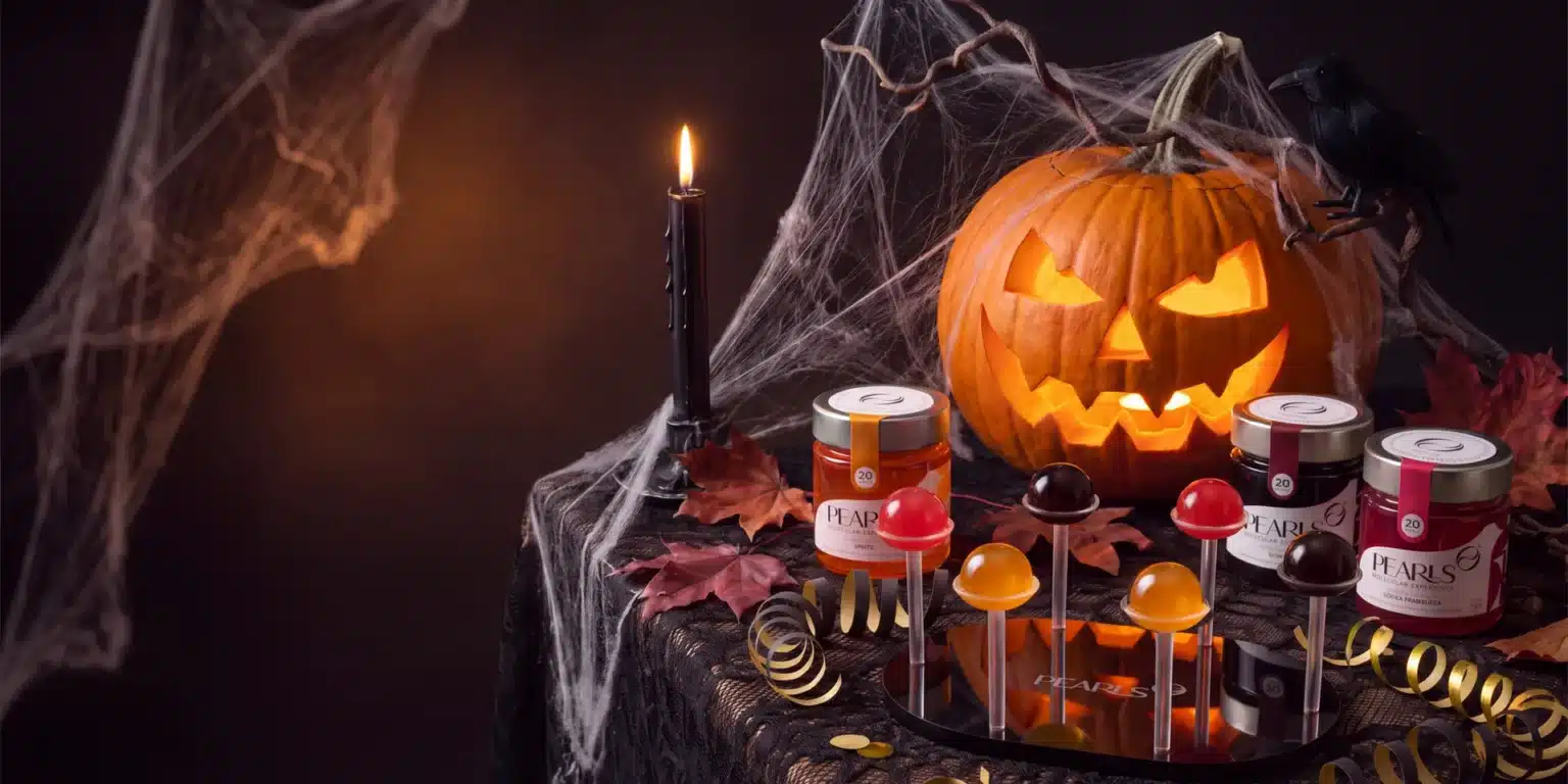 Mesa de Halloween con calabaza tallada y Pearls de Spritz, Ron Café y Vodka Frambuesa en soportes, junto a sus frascos